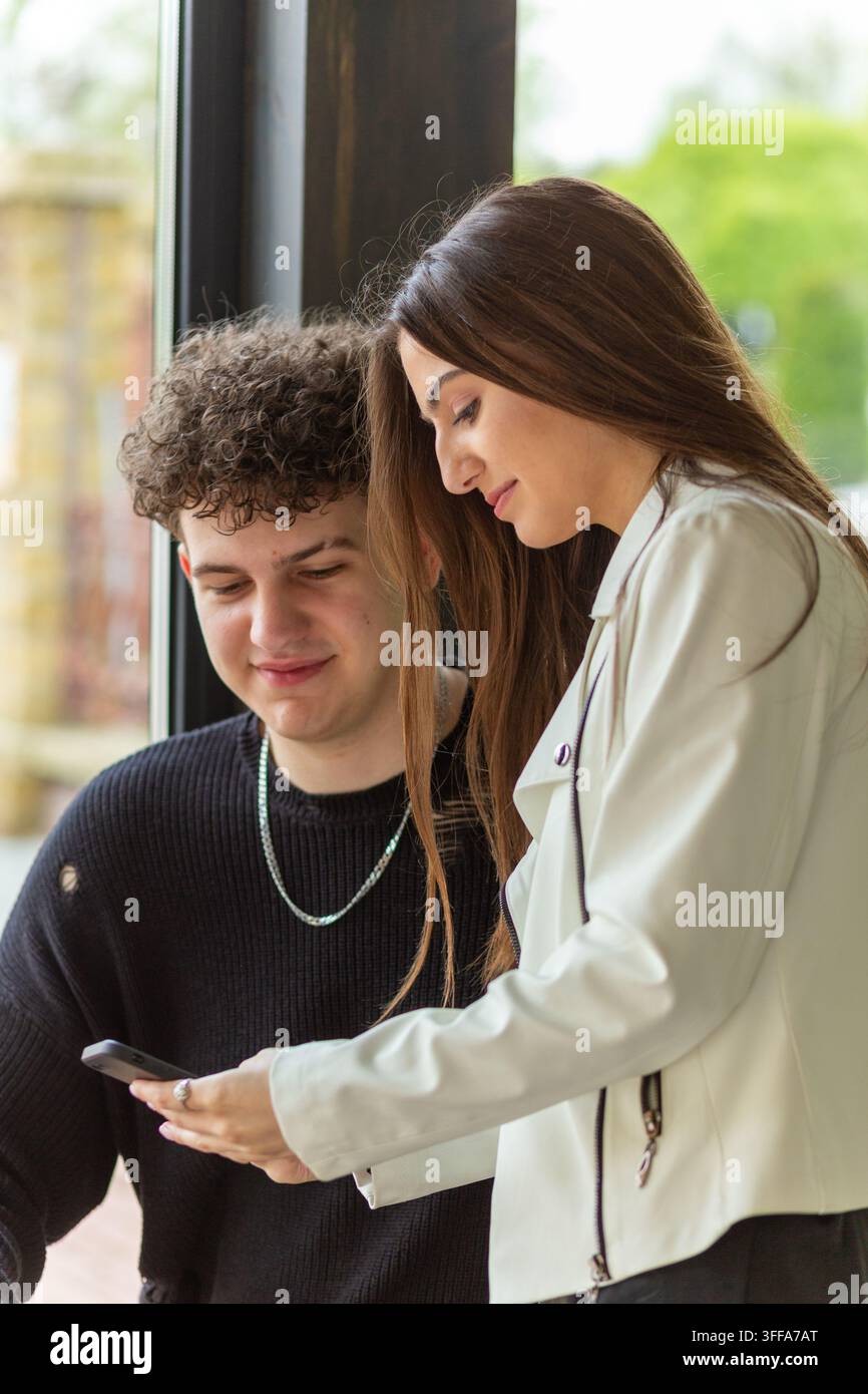 , sorridono insieme mentre una donna controlla il suo smartphone su uno sfondo verde sfocato all'aperto. Foto Stock