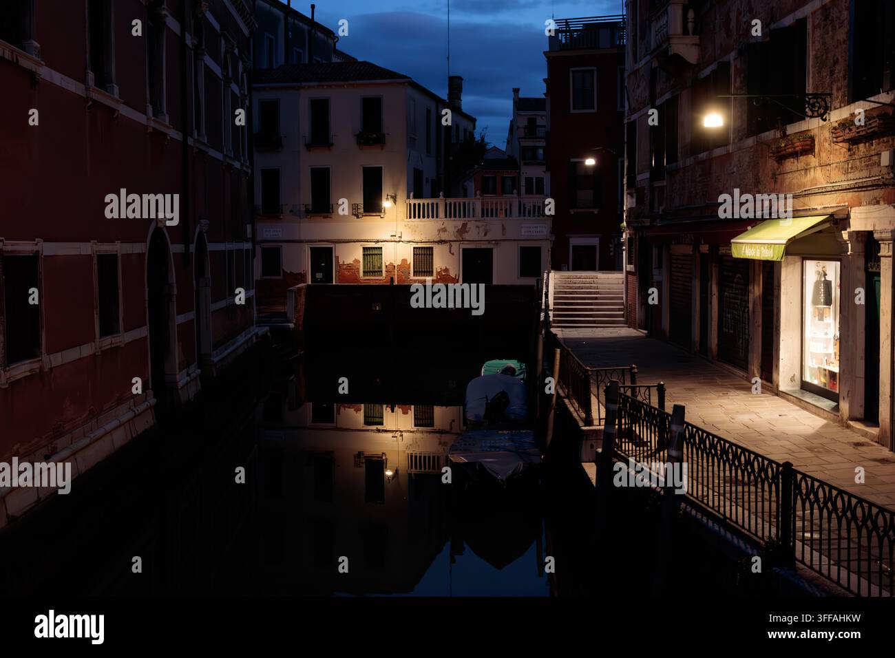 Canale stretto veneziano debolmente illuminato e fondamenta di notte con luci calde da strada, Venezia, Italia Foto Stock