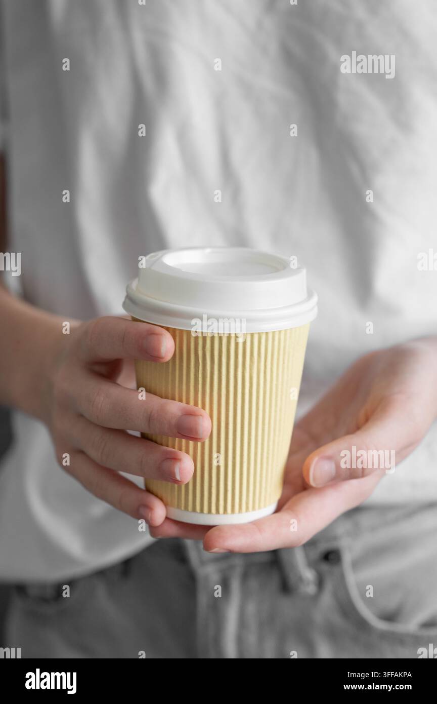 Mani femminili che tengono una tazza di carta con caffè su uno sfondo neutro morbido. Concetto di routine mattutina e bevande da asporto. Spazio per la copia. Foto Stock