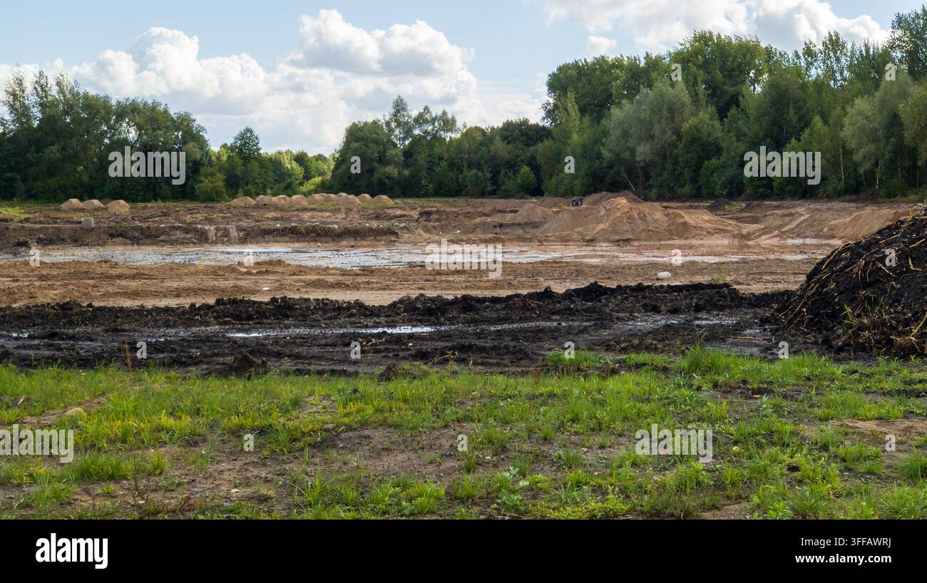 Cantiere edile livellato con cumuli di terreno scavati. Ampia area di terreno appiattita circondata da foresta verde sotto un cielo nuvoloso. Concetto di preparazione del terreno Foto Stock