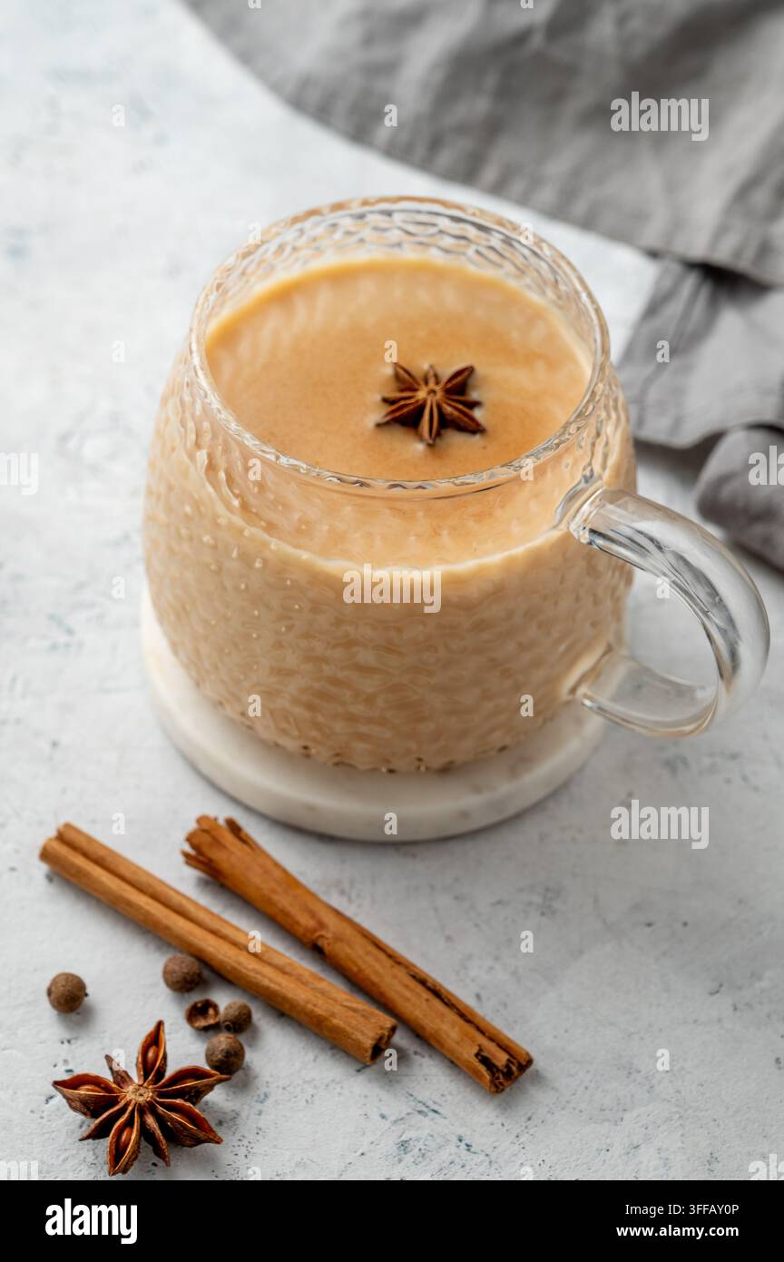Tè masala chai indiano tradizionale con latte e spezie in una tazza su uno sfondo chiaro con cannella, anice e tovagliolo. Un concetto di bevanda calda accogliente per un Foto Stock