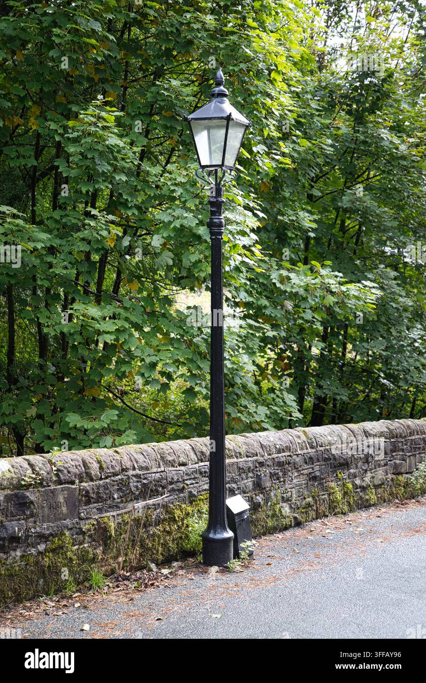 Classico lampione vintage nero accanto a un vecchio muro di pietra coperto di muschio lungo Barrow Bridge Road a Bolton, Greater Manchester, Regno Unito. Foto Stock