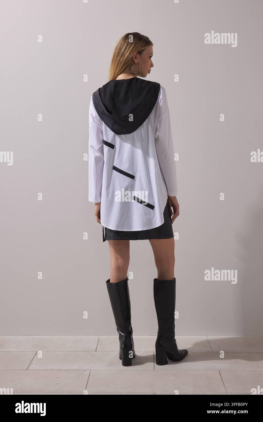 Giovane donna bionda che indossa una camicia oversize a blocchi di colore bianco e nero con un design grafico audace, abbinata a una minigonna nera. Foto Stock