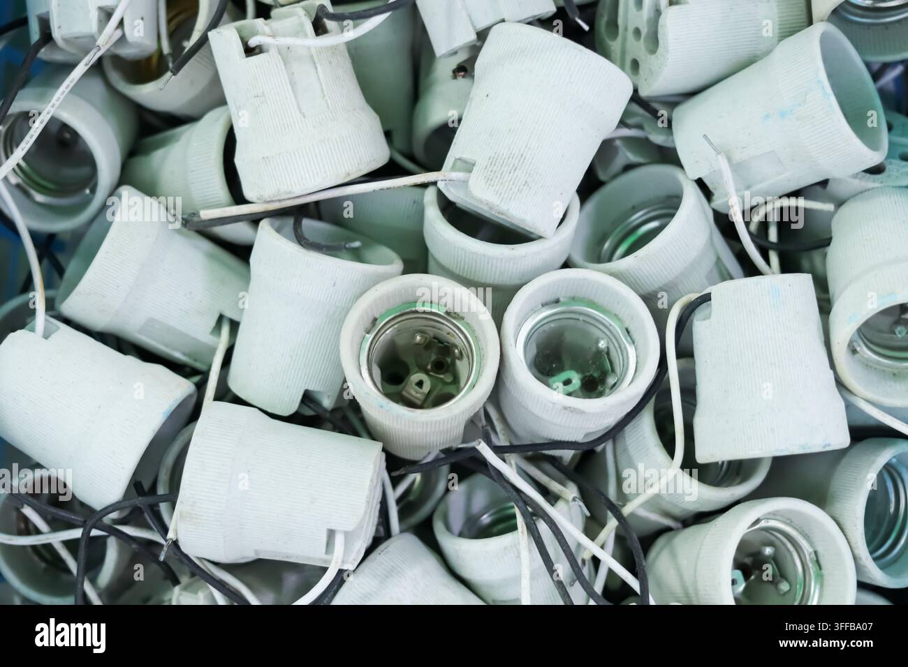 Portalampe in ceramica bianca usati con fili neri e bianchi tagliati ammucchiati in un mucchio, primo piano aereo di scarti elettrici per il riciclo Foto Stock
