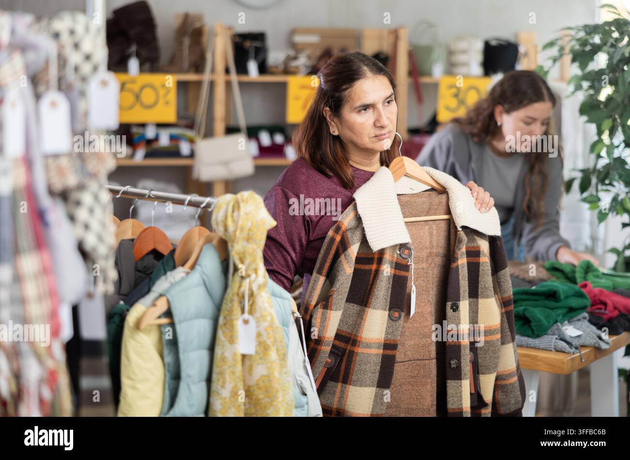 Donna fashionista vicino a una vetrina esamina i prodotti, acquista una giacca a quadri. Negozio di abbigliamento fuori linea di un rivenditore. Look di stile e moda, moder Foto Stock