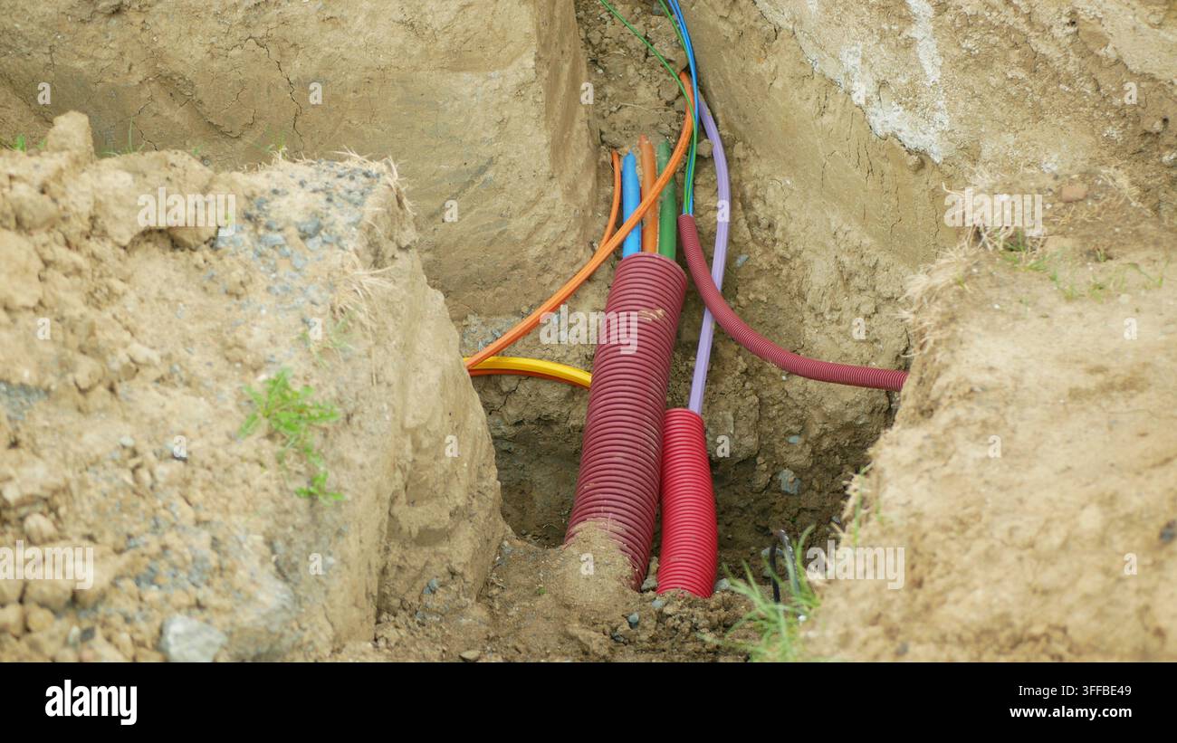 Rete di ingegneria Internet in fibra ottica infrastrutture cavi condotti in rame posati installati sottoterra trincea di terreno scavata costruzione Foto Stock