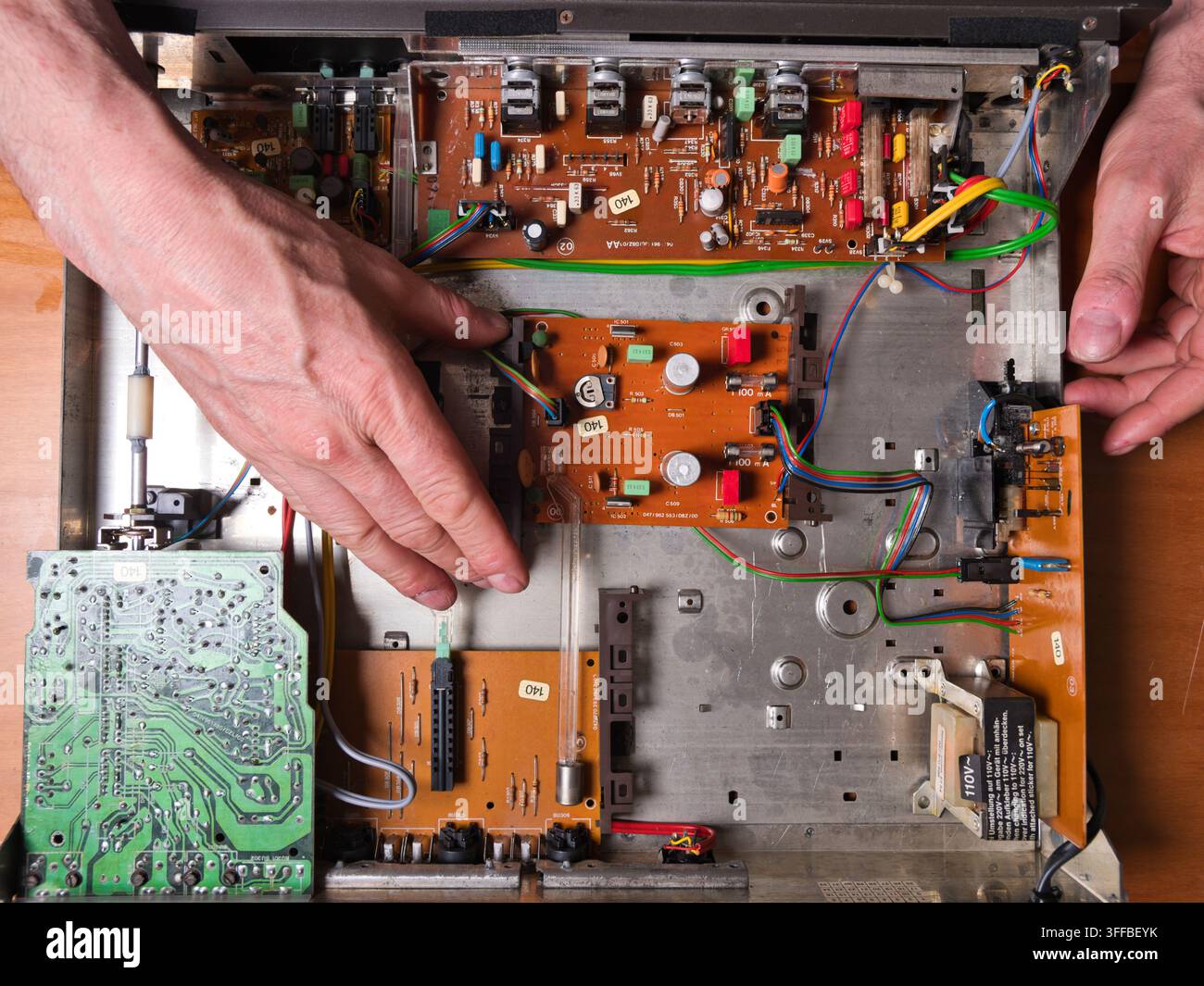Mani che lavorano su un circ elettronico vintage - Vista dall'alto delle mani di una persona che ripara i componenti interni di un vecchio dispositivo elettronico, con Foto Stock