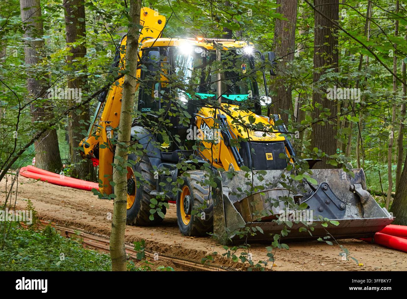 Mosca, Russia - 04 settembre 2026: Escavatore JCB in un ambiente boschivo, impegnato in lavori di pipeline con tubi rossi posati a terra Foto Stock