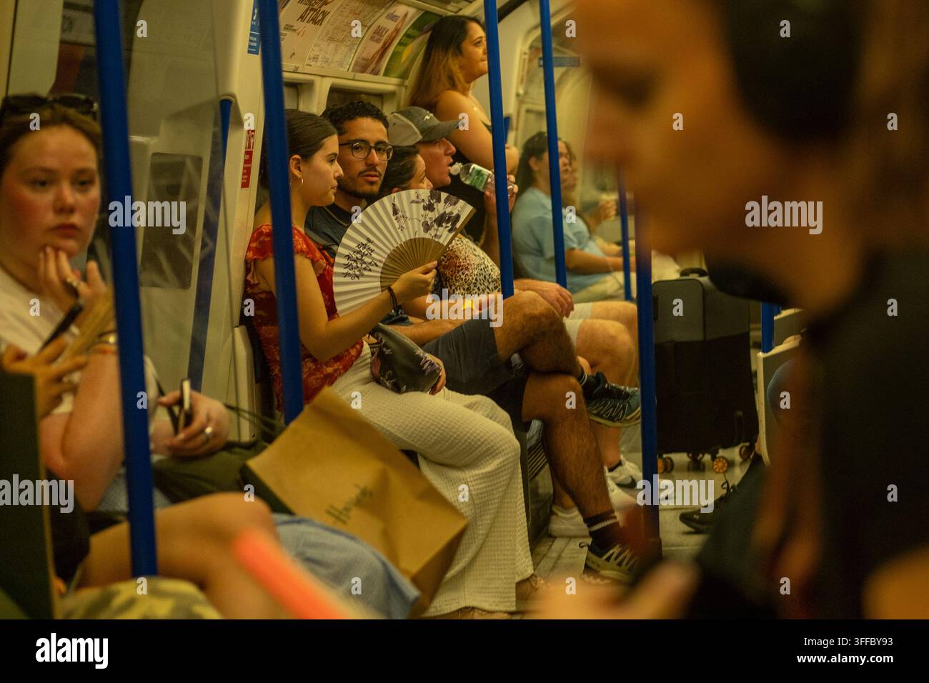 LONDRA – 25 GIUGNO 2026: Northern line tube – Passeggeri che usano un ventaglio portatile durante l’ondata di caldo estiva. Foto Stock