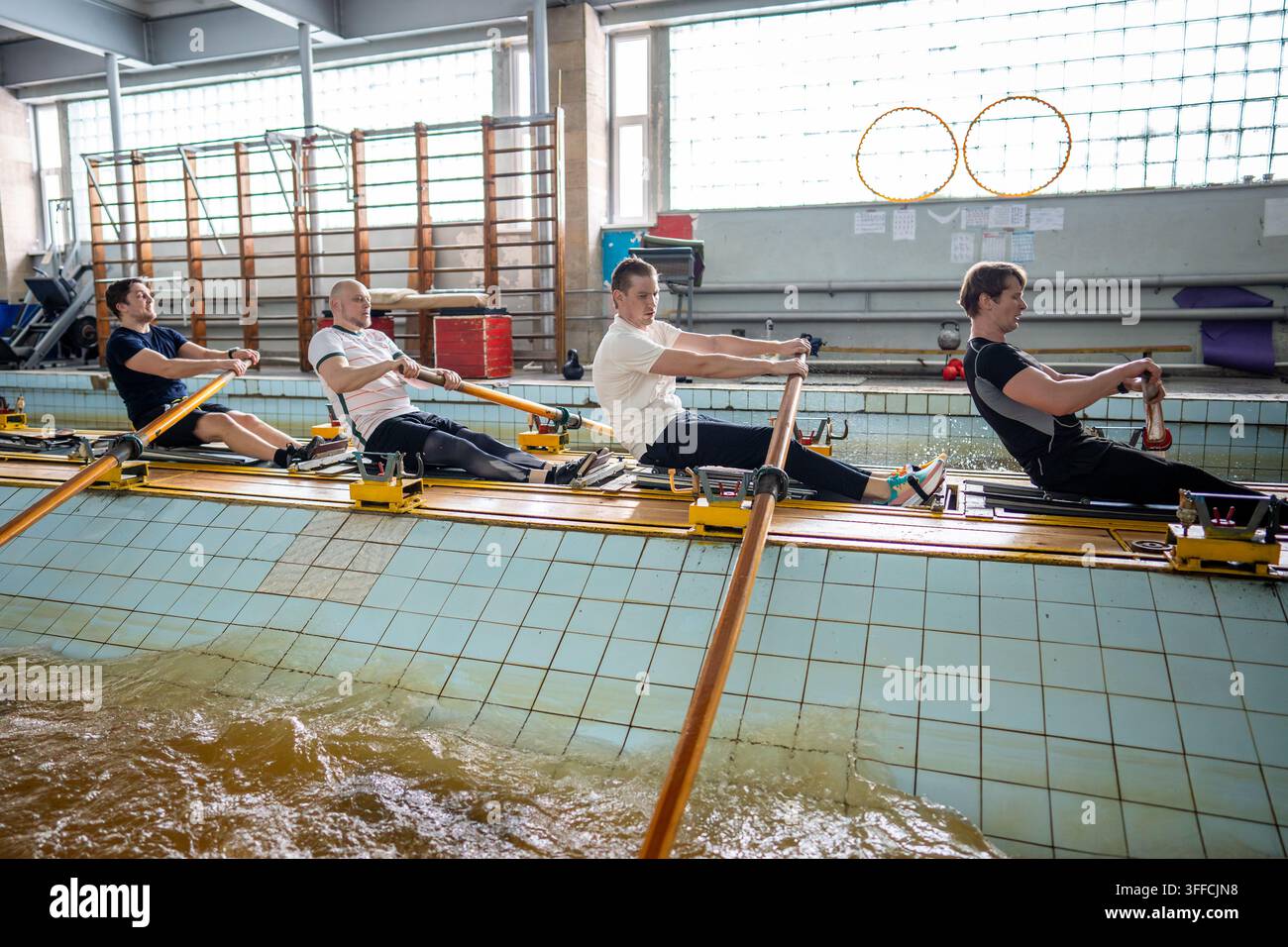 Squadra maschile di canottaggio concentrata che mantiene colpi sincronizzati durante un allenamento intensivo indoor sulla macchina ergometrica Foto Stock