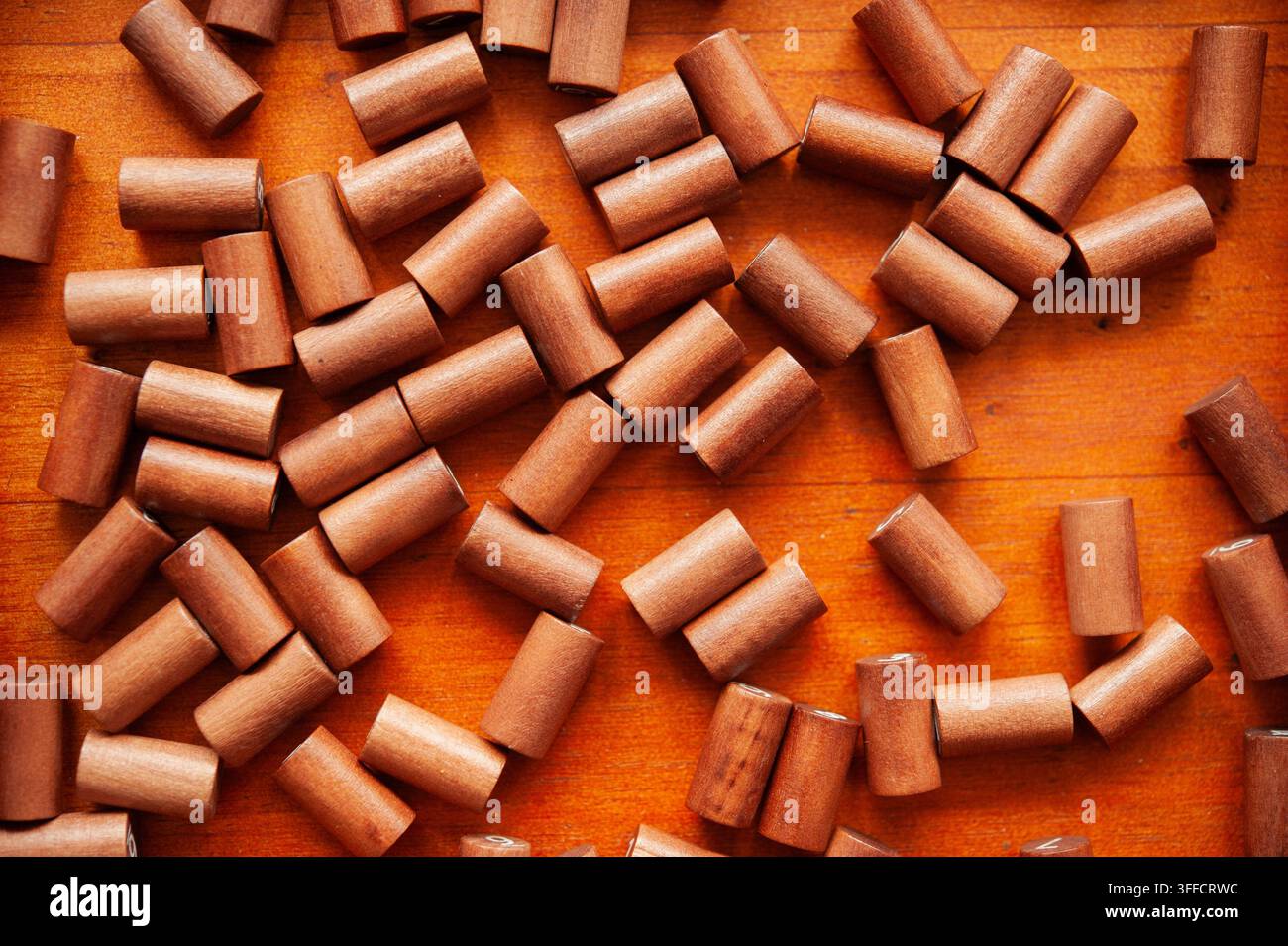 Piccoli pezzi di gioco cilindrici in legno sparsi su una superficie di legno calda, che suggeriscono un puzzle tattile, un gioco di conteggio o un gioco da tavolo tradizionale Foto Stock