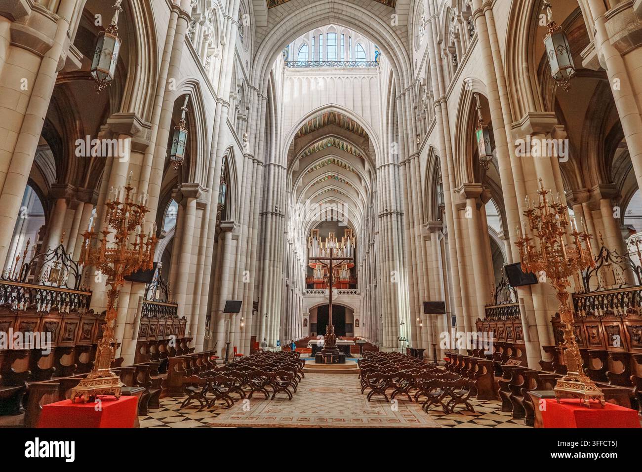 Madrid, Spagna: 7 apr. 2025 – Stalli di coro in legno ornati e alti candelabri dorati delimitano una navata di marmo a scacchi che conduce verso un crocifisso lontano e Foto Stock
