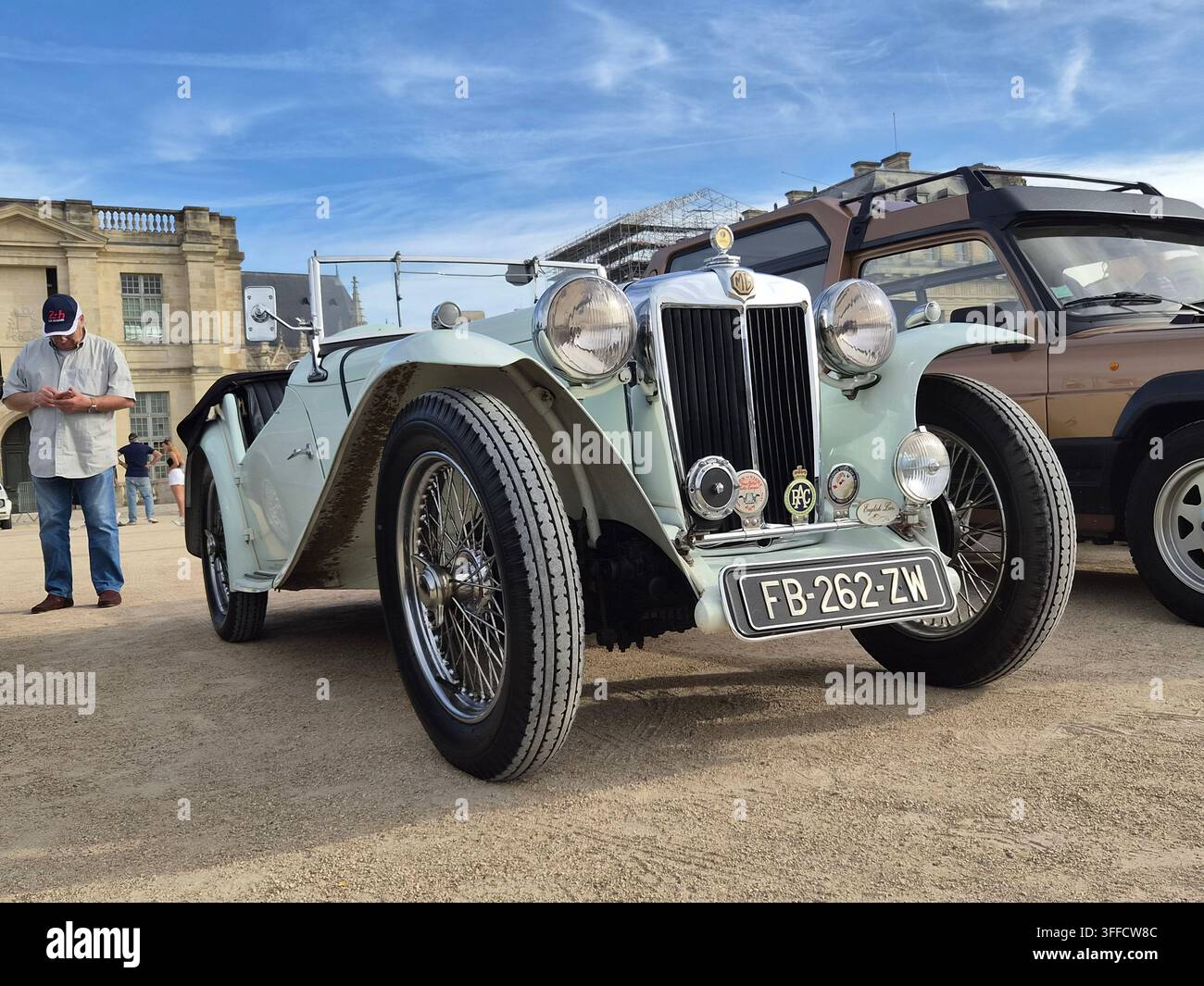 Vista frontale a basso angolo di un classico roadster MG vintage bianco parcheggiato in una mostra all'aperto con un edificio storico in pietra sullo sfondo. Foto Stock