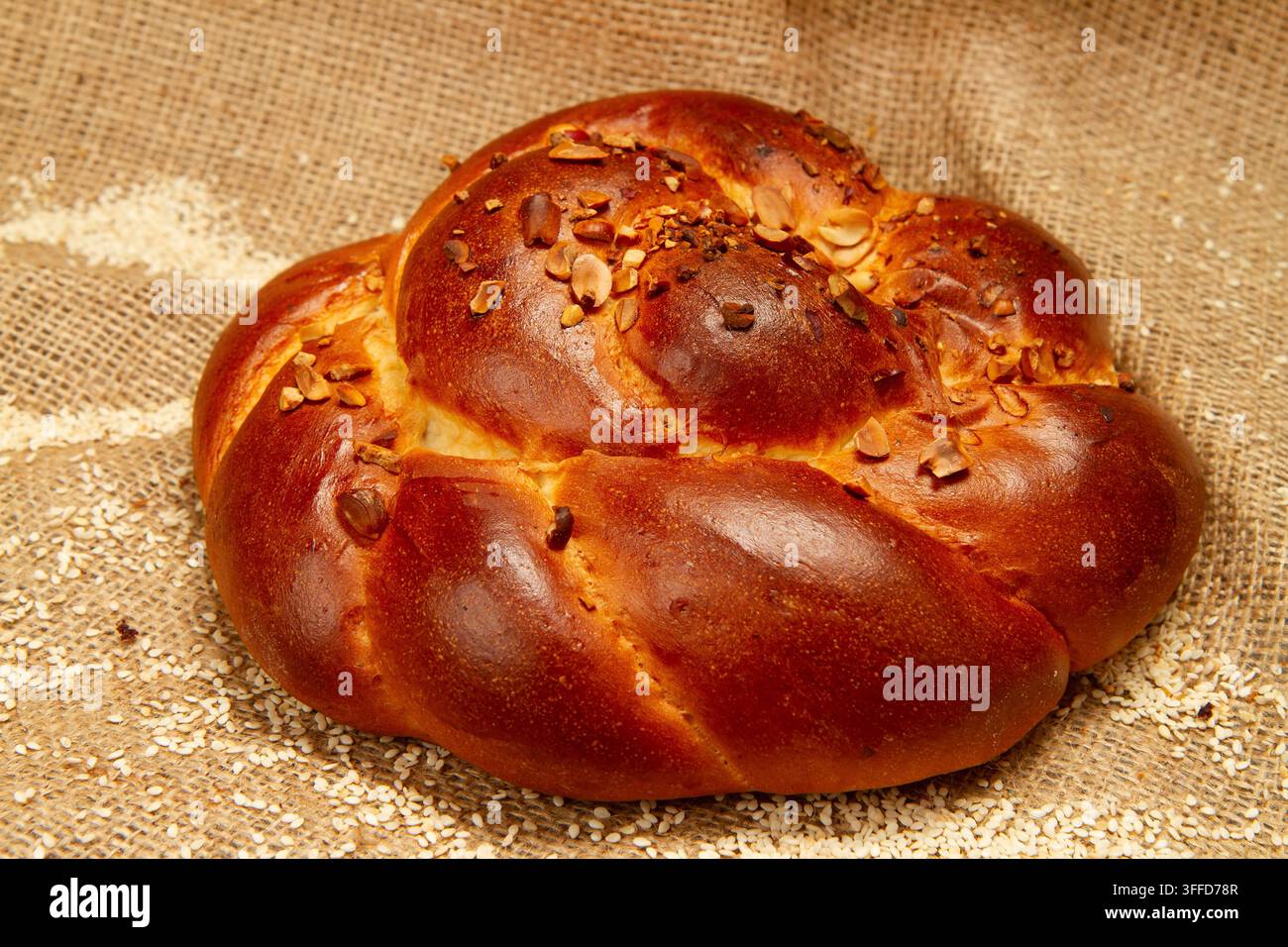 Panino dolce e burroso. Prodotto da forno sullo sfondo di tela di sacco. Panino con sesamo e noci in primo piano. Foto Stock