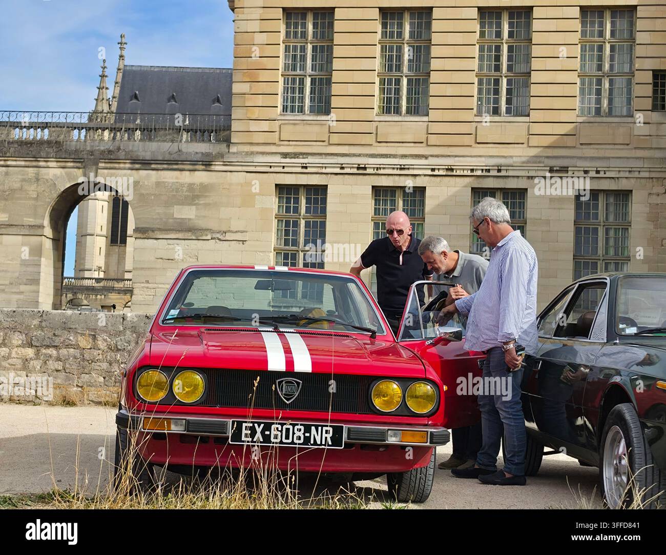 Uomini che ispezionano una classica auto sportiva Lancia Fulvia Coupé rossa con strisce da corsa bianche parcheggiata fuori dal Château de Vincennes durante un raduno di auto d'epoca Foto Stock