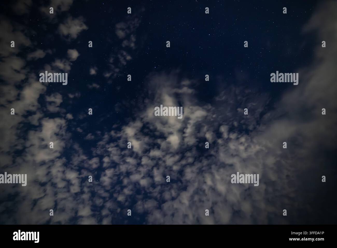 Vista grandangolare di un cielo notturno scuro pieno di stelle e nuvole illuminate. La vasta distesa blu profondo mostra un paesaggio celeste dinamico con nuvole strutturate. Foto Stock
