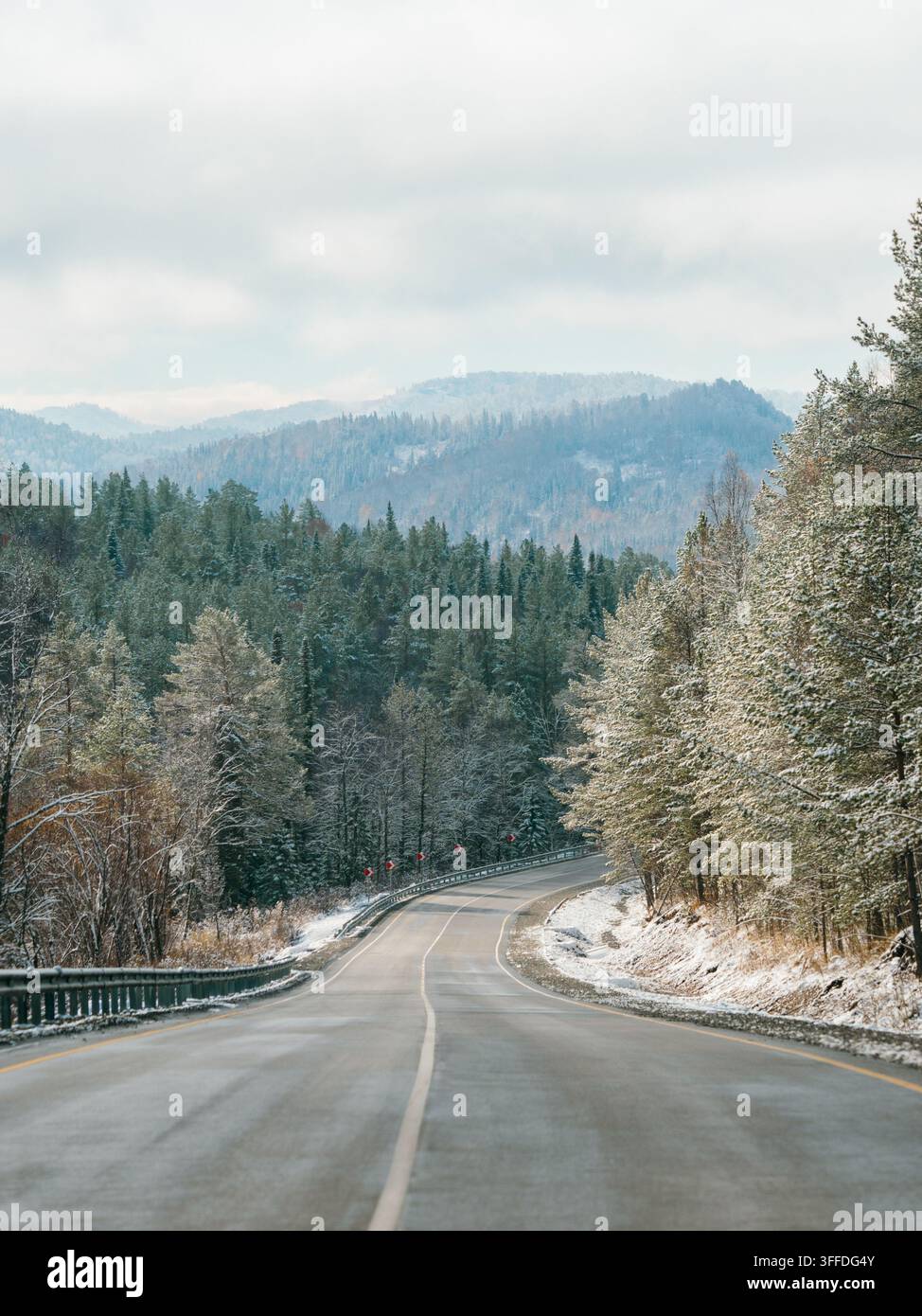Strada invernale tra montagne innevate. Autunno o inverno in montagna. Strada asfaltata attraverso una foresta di abeti e bianchi picchi innevati in lontananza sullo sfondo. Paesaggio straordinario. Spazio di copia Foto Stock