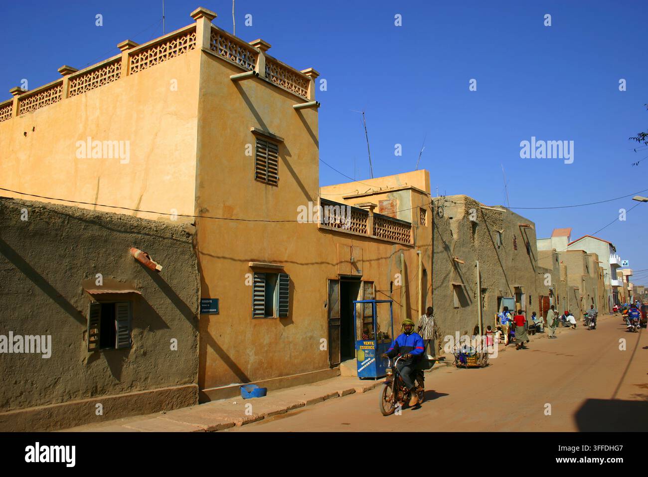 Una strada affollata a Mopti, Mali, che mostra edifici in terra, motociclette, pedoni, commercio lungo la strada e cieli blu brillanti. Foto Stock