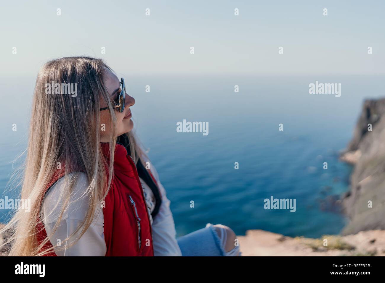 Vista da una scogliera oceanica di una giovane viaggiatrice seduta su un bordo roccioso e che guarda l'orizzonte del mare Foto Stock