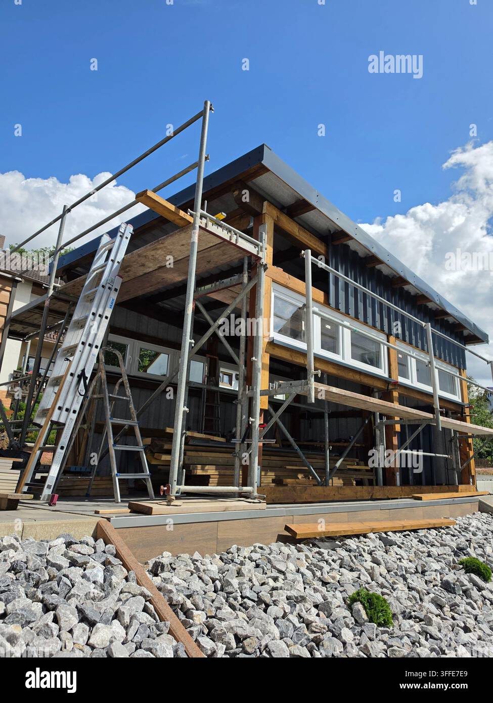 Edificio residenziale moderno in costruzione con impalcatura metallica e scala su sfondo di cielo blu con nuvole bianche in Germania - Immagine stock catturata con smartphone