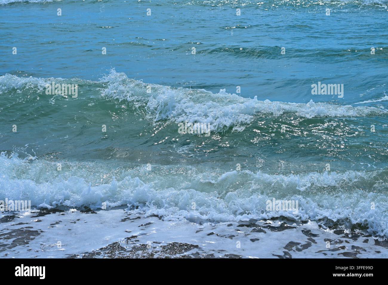 Primo piano di onde turchesi che si infrangono su sabbia bagnata con schiuma bianca Foto Stock
