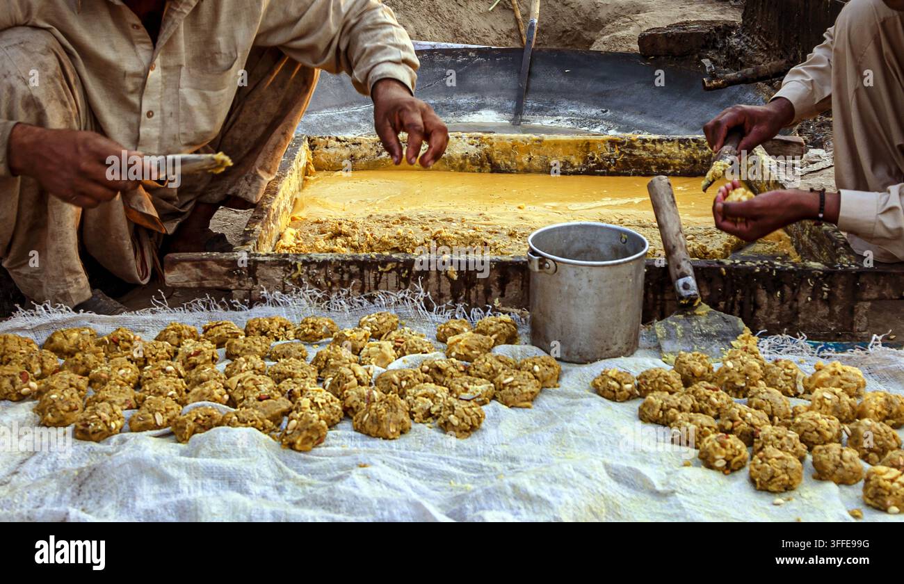 Vista di operai che modellano il jaggery tradizionale in piccole palline da una grande padella a Multan, Punjab, Pakistan. Foto Stock