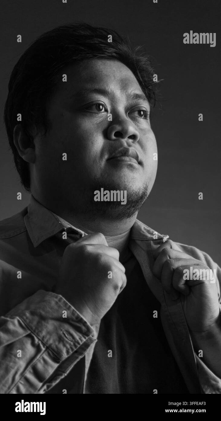 Ritratto in bianco e nero di un giovane uomo asiatico che guarda verso l'alto e lontano dalla fotocamera con un'espressione pensierosa e contemplativa. Il soggetto è gr Foto Stock