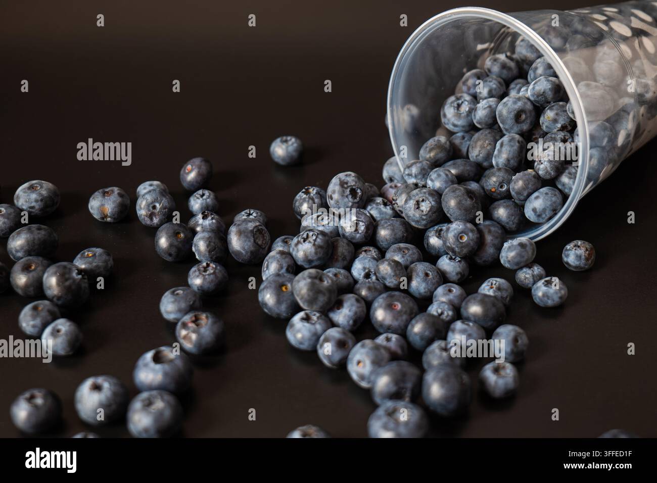 Una tazza trasparente poggia su un lato con enfasi sull'apertura e sulle bacche vicine. La prospettiva angolata evidenzia profondità, texture e abbondanza. Foto Stock