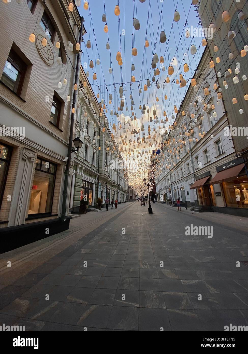 Mosca, Russia - 15 agosto 2022: un'installazione di lanterne sospese si estende sulla strada pedonale dei negozi nella morbida luce del crepuscolo. - Immagine stock catturata con smartphone
