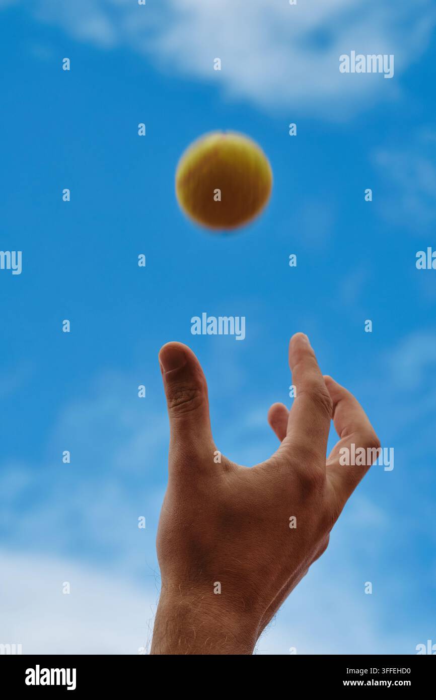 Primo piano di una mano maschile che lancia una pallina da tennis in aria Foto Stock