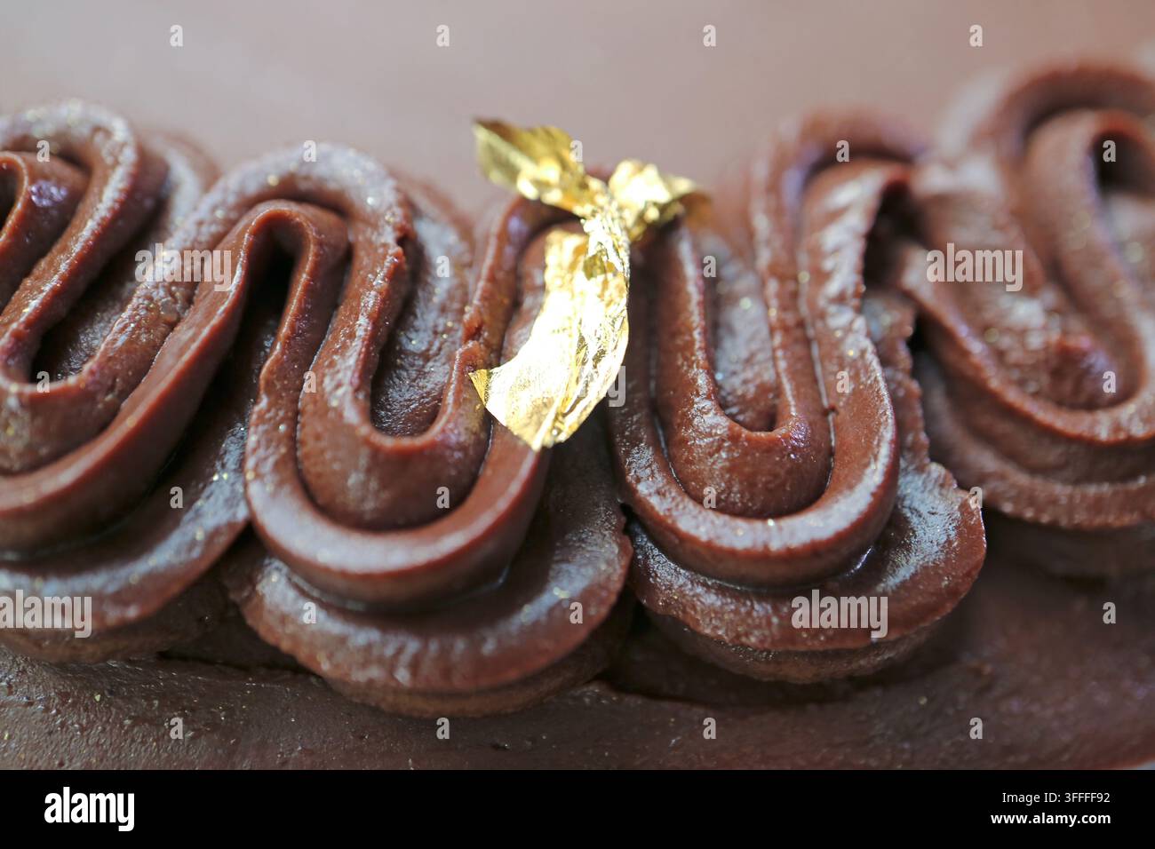 Macro di una deliziosa glassa ganache al cioccolato fondente su una torta decorata con foglia d'oro commestibile di alta qualità Foto Stock