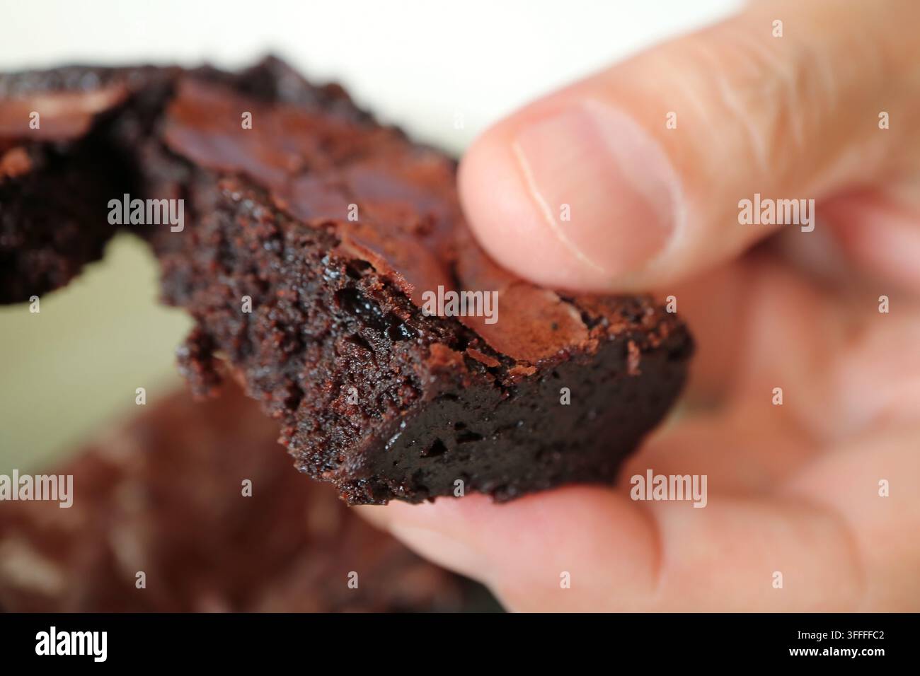 Dita di un uomo che spezzano un pezzo di brownie al cioccolato ricco e morbido, mostrando la sua consistenza umida Foto Stock