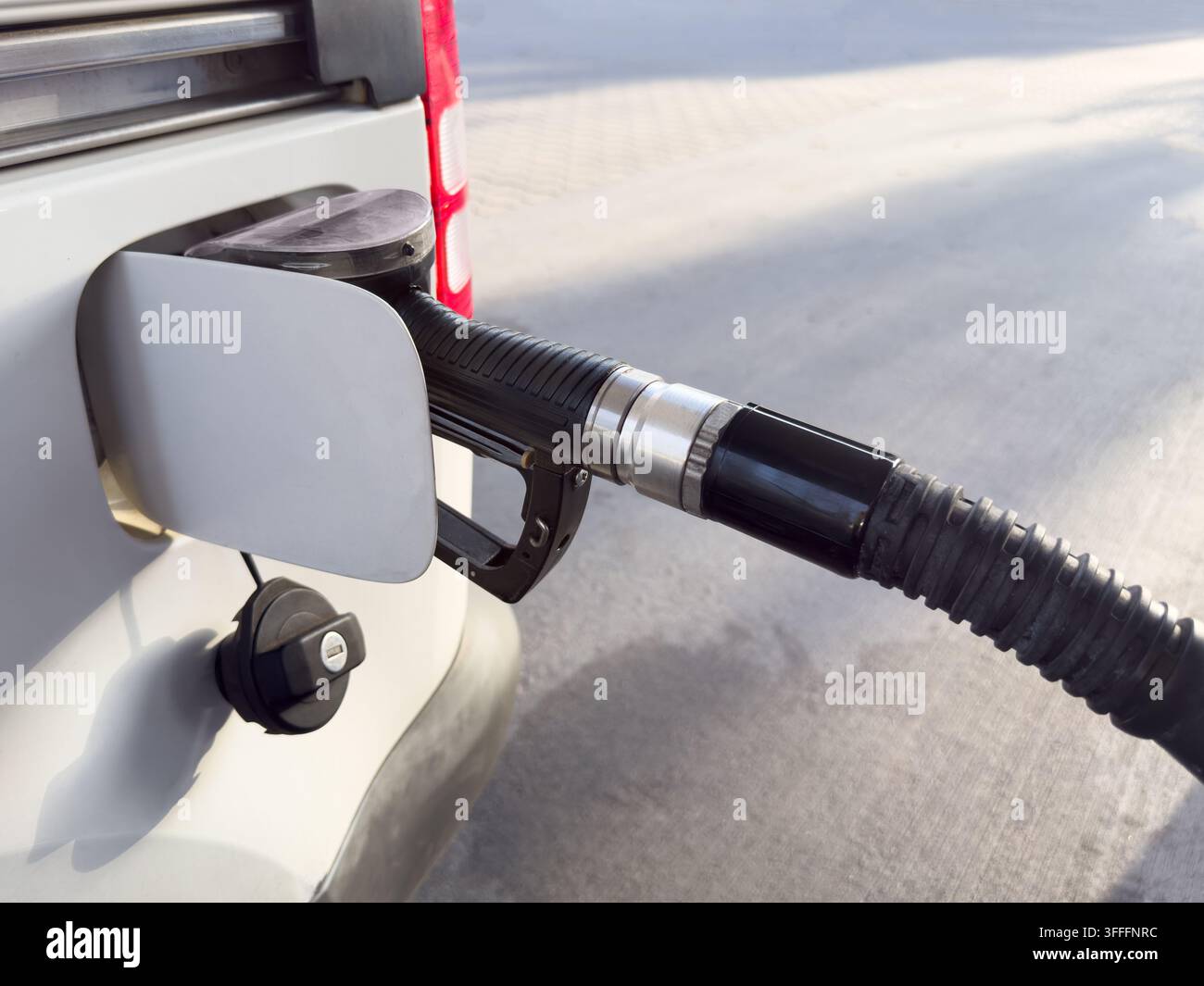 Prima di un erogatore di carburante che rifornisce un'auto in una stazione di servizio, illustrando i prezzi del carburante, l'aumento dei costi di trasporto, l'inflazione, le spese energetiche e la casa - Immagine stock catturata con smartphone