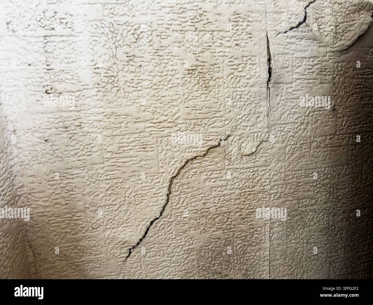 Immagine di un muro interno di una casa rivestito di carta da parati vecchia, parzialmente ceduto, che mostra una notevole crepa nel muro e macchie di umidità e muffa Foto Stock