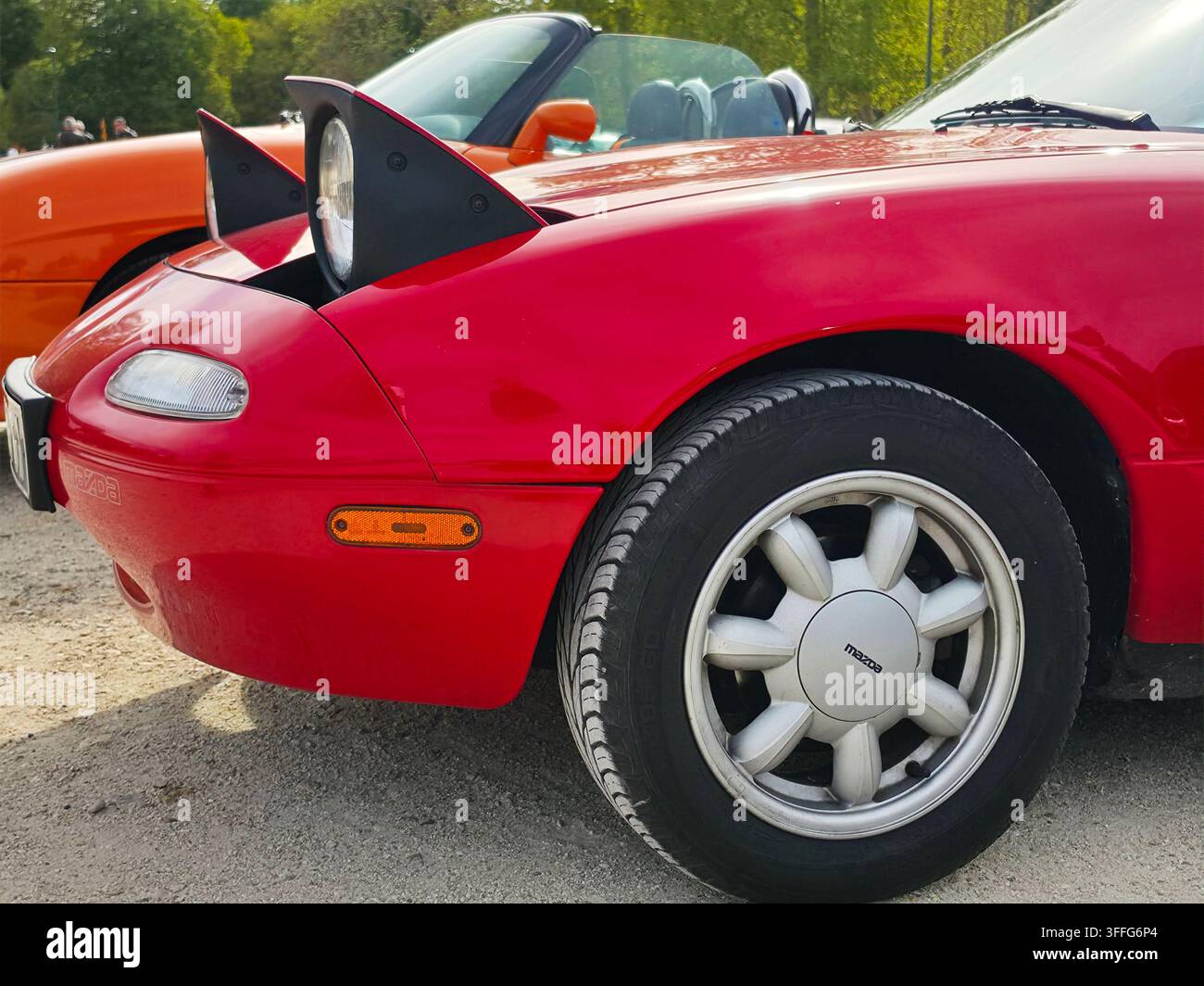 Prima vista ravvicinata del quarto anteriore di un'auto sportiva Mazda MX-5 Miata di prima generazione rosso acceso con fari pop-up dispiegati in mostra Foto Stock