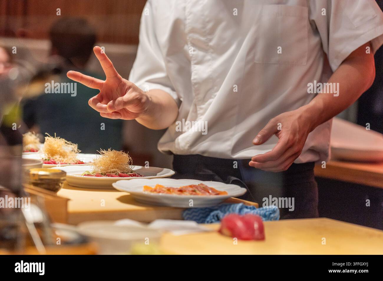 Lo chef prepara piatti di sushi con stile artistico in una cucina di ristorante vivace, mostrando abilità culinarie e creatività. Foto Stock