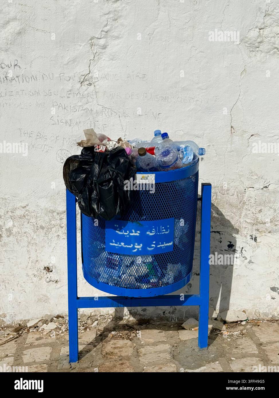 Cestino pubblico straripante a Sidi Bou Said, Tunisia, che illustra la pressione nella gestione dei rifiuti e le sfide ambientali associate al turismo intensivo - Immagine stock catturata con smartphone