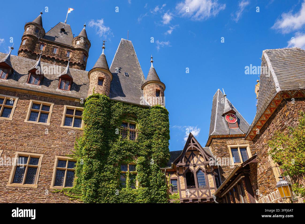 Castello medievale di Reichsburg Cochem con mura di pietra ricoperte di edera, guglie e torrette sotto un cielo blu brillante in Germania Foto Stock