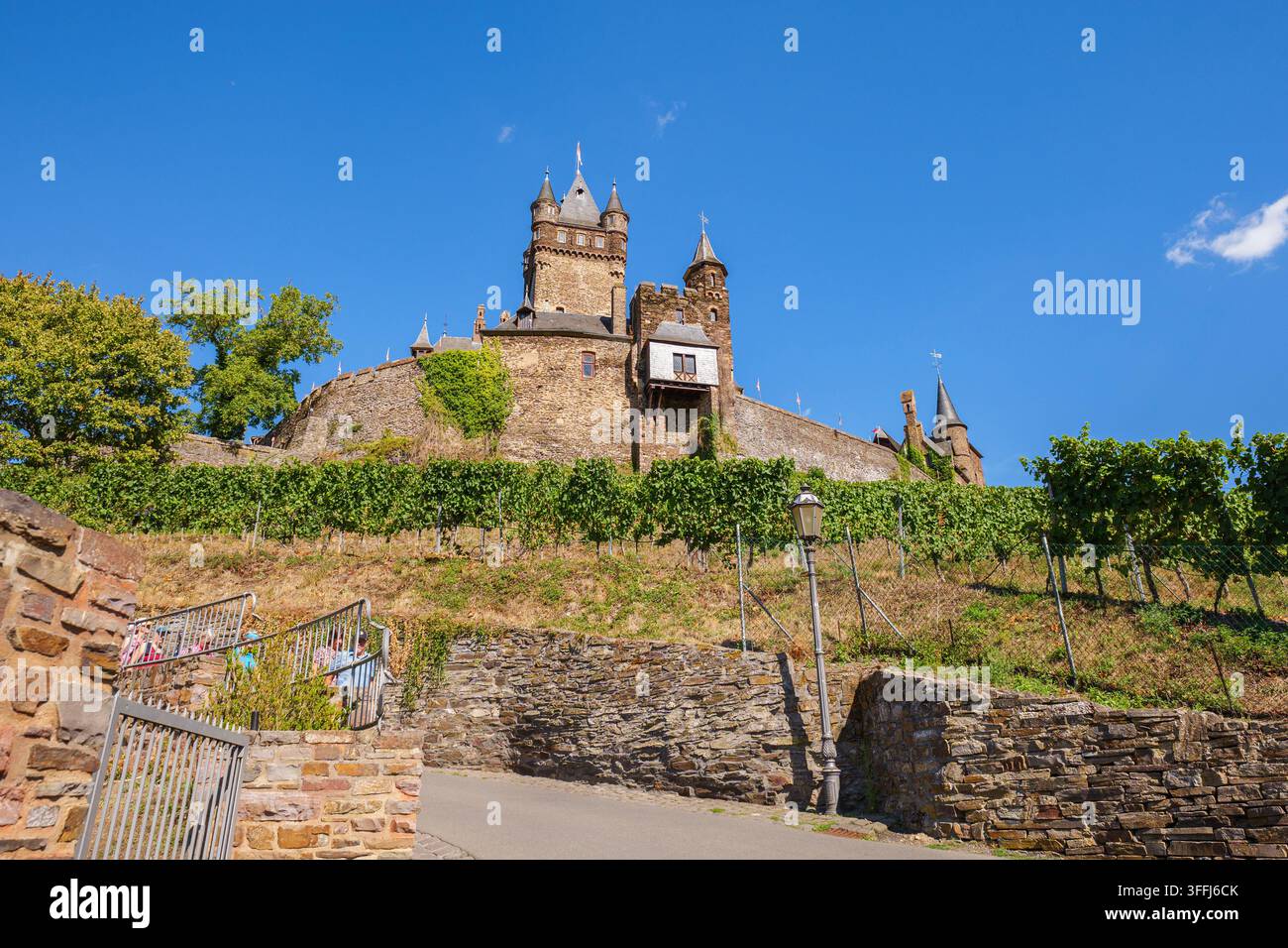 Castello architetttura storica medievale fortezza su una collina con vigneti, mura di pietra e un sentiero sotto un cielo blu Foto Stock