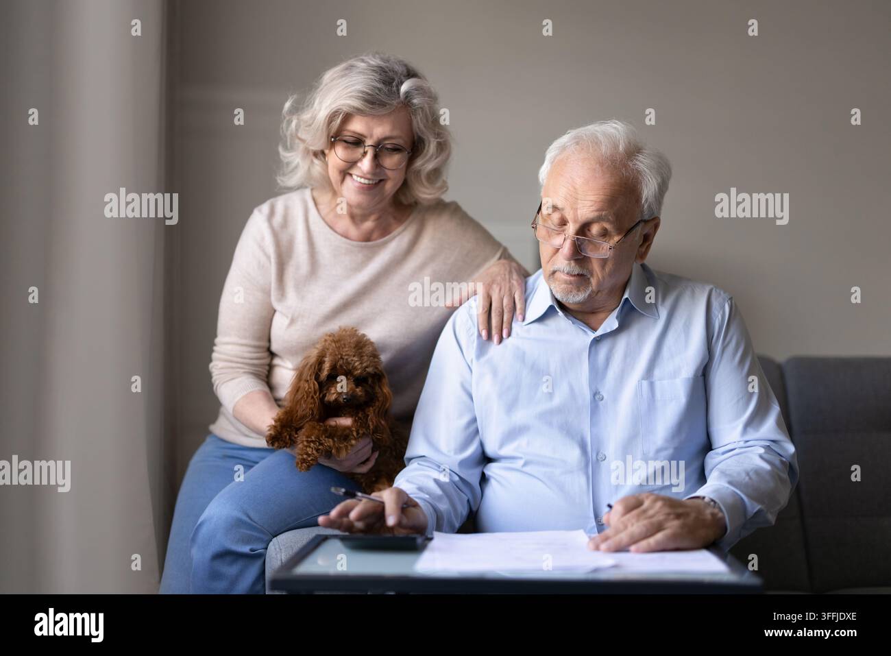 Coppia di anziani che gestisce il budget familiare seduta sul divano con il cane Foto Stock