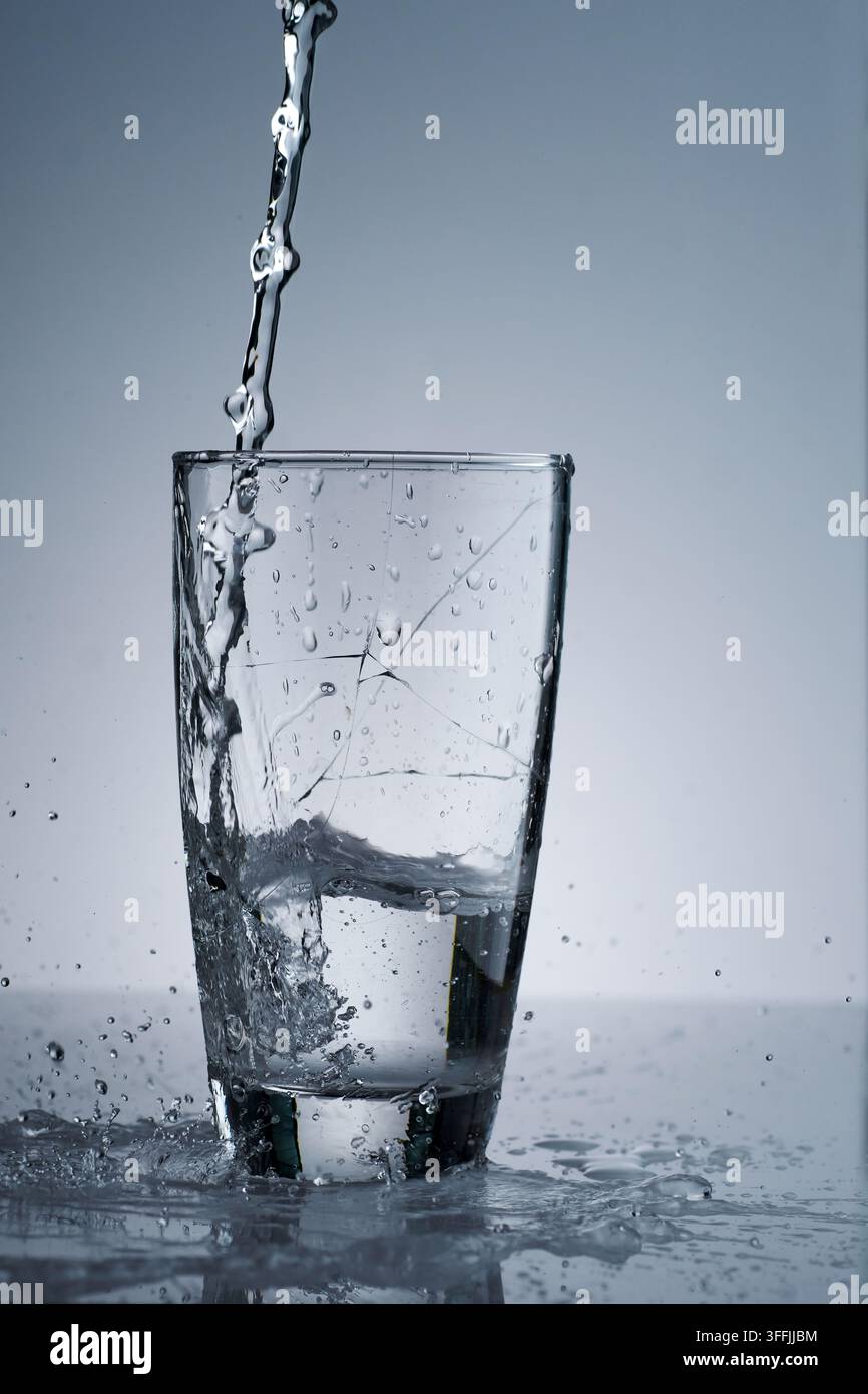 versa acqua potabile fresca in modo violento che fece rompere un bicchiere e cadere una parte Foto Stock