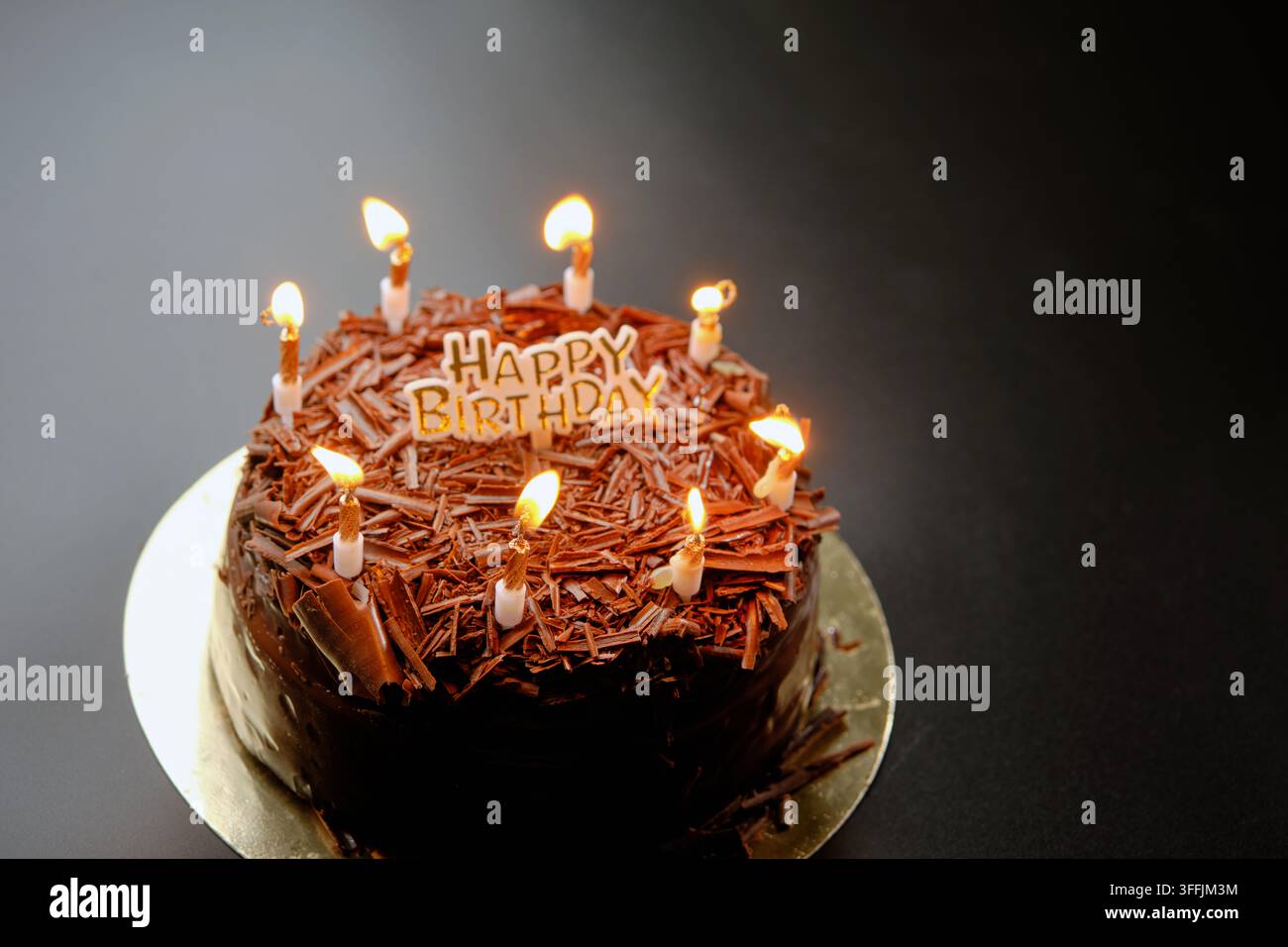 Una torta di cioccolato nero scuro con un cartello Happy Birthday si trova su uno sfondo nero Foto Stock