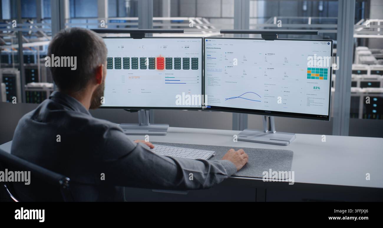 Specialista IT monitora l'infrastruttura dei server su due schermi dopo un allarme critico di surriscaldamento, risolve i problemi dei sistemi del data center per prevenire danni ai dispositivi, tempi di inattività e interruzioni del servizio. Foto Stock