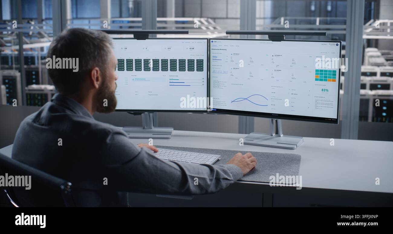 Specialista IT monitora l'infrastruttura dei server su due schermi dopo un allarme critico di surriscaldamento, risolve i problemi dei sistemi del data center per prevenire danni ai dispositivi, tempi di inattività e interruzioni del servizio. Foto Stock