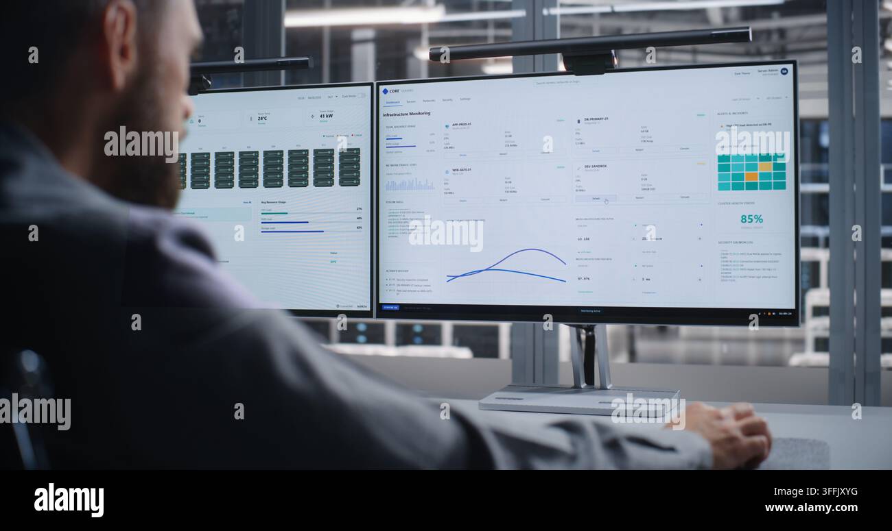 Professionista IT indaga un errore critico del sistema all'interno di un data center, utilizzando due monitor per analizzare le prestazioni dell'infrastruttura, risolvere i problemi dei server, mantenere l'affidabilità e prevenire tempi di inattività. Foto Stock