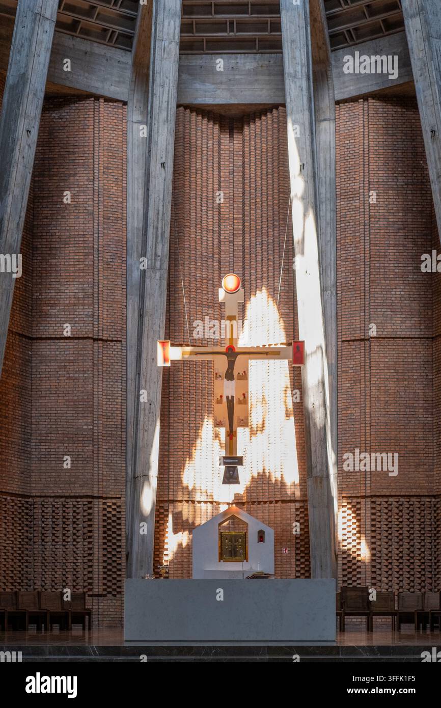 Un crocifisso di legno sospeso pende sopra un altare di pietra all'interno di un moderno interno di chiesa in mattoni e cemento. Foto Stock