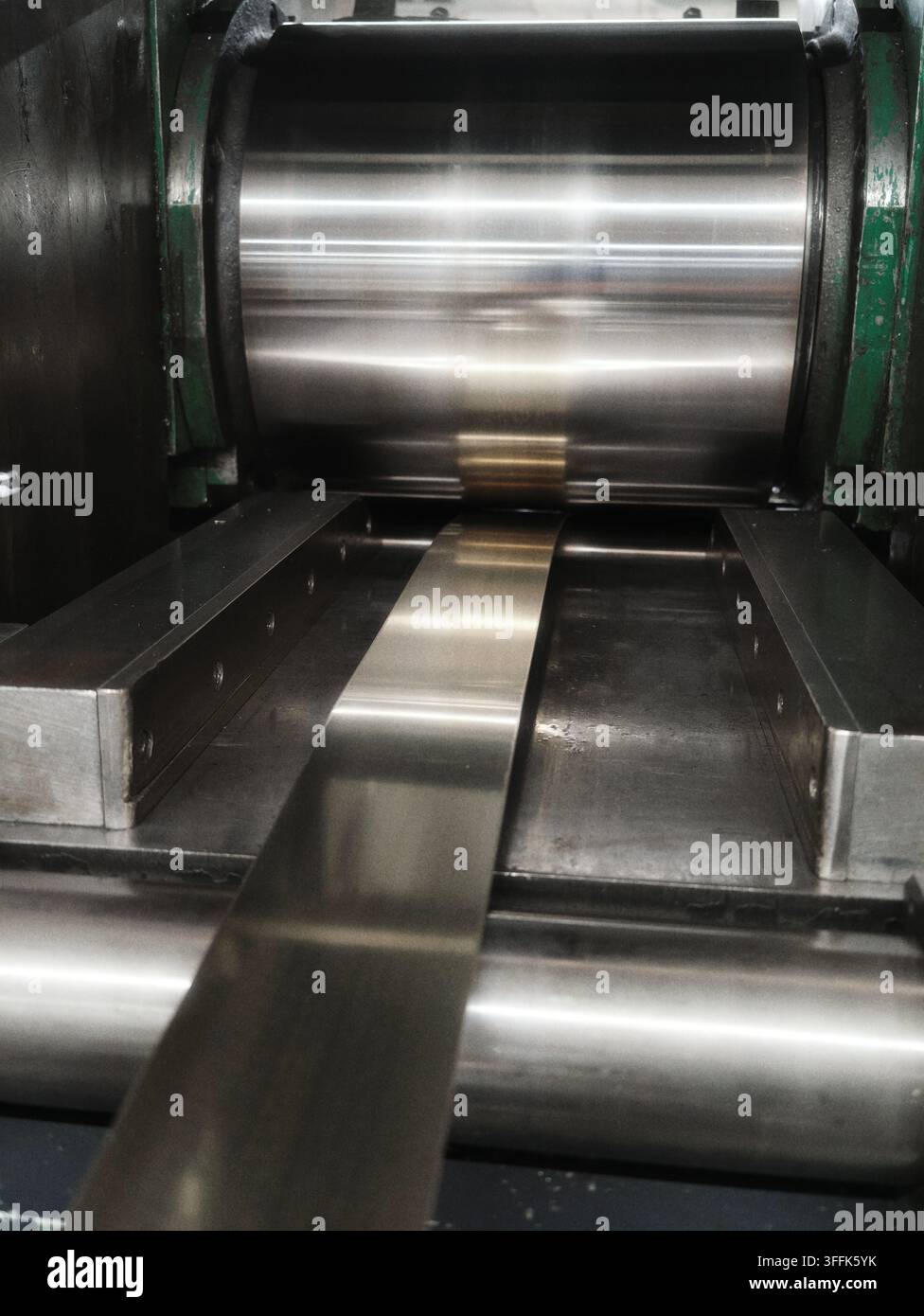 Striscia di lamiera metallica lucida che si sposta attraverso macchinari di laminazione dell'acciaio in una moderna fabbrica, vista ravvicinata di attrezzature pesanti Foto Stock