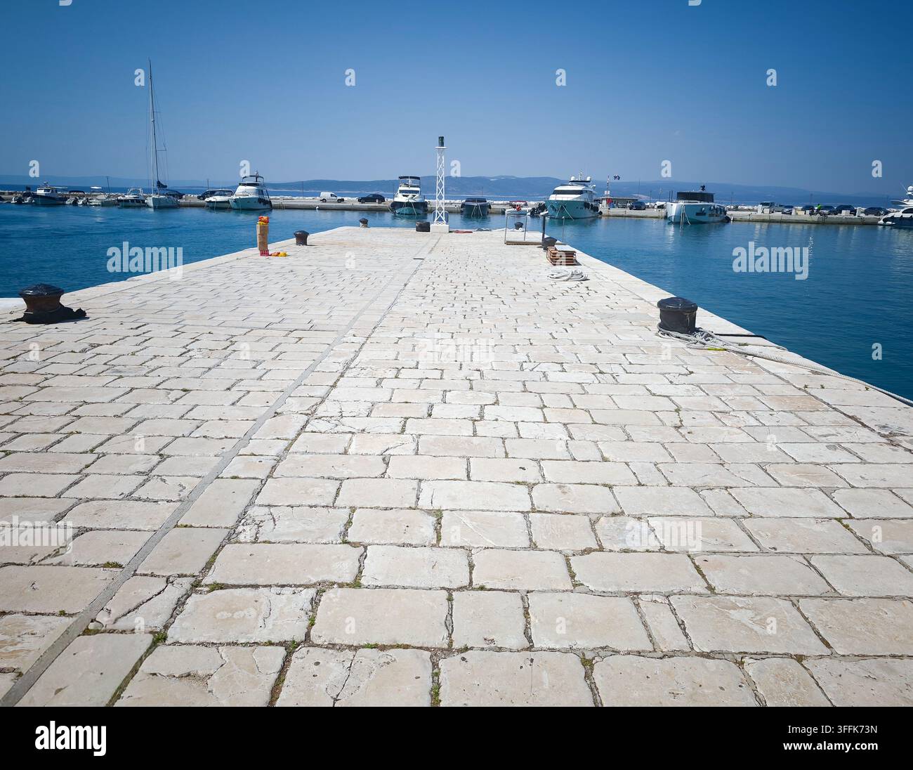 Un piano grandangolare di un molo lastricato di pietra che si estende nel mare azzurro con yacht ormeggiati nel porto di Baska Voda. - Immagine stock catturata con smartphone