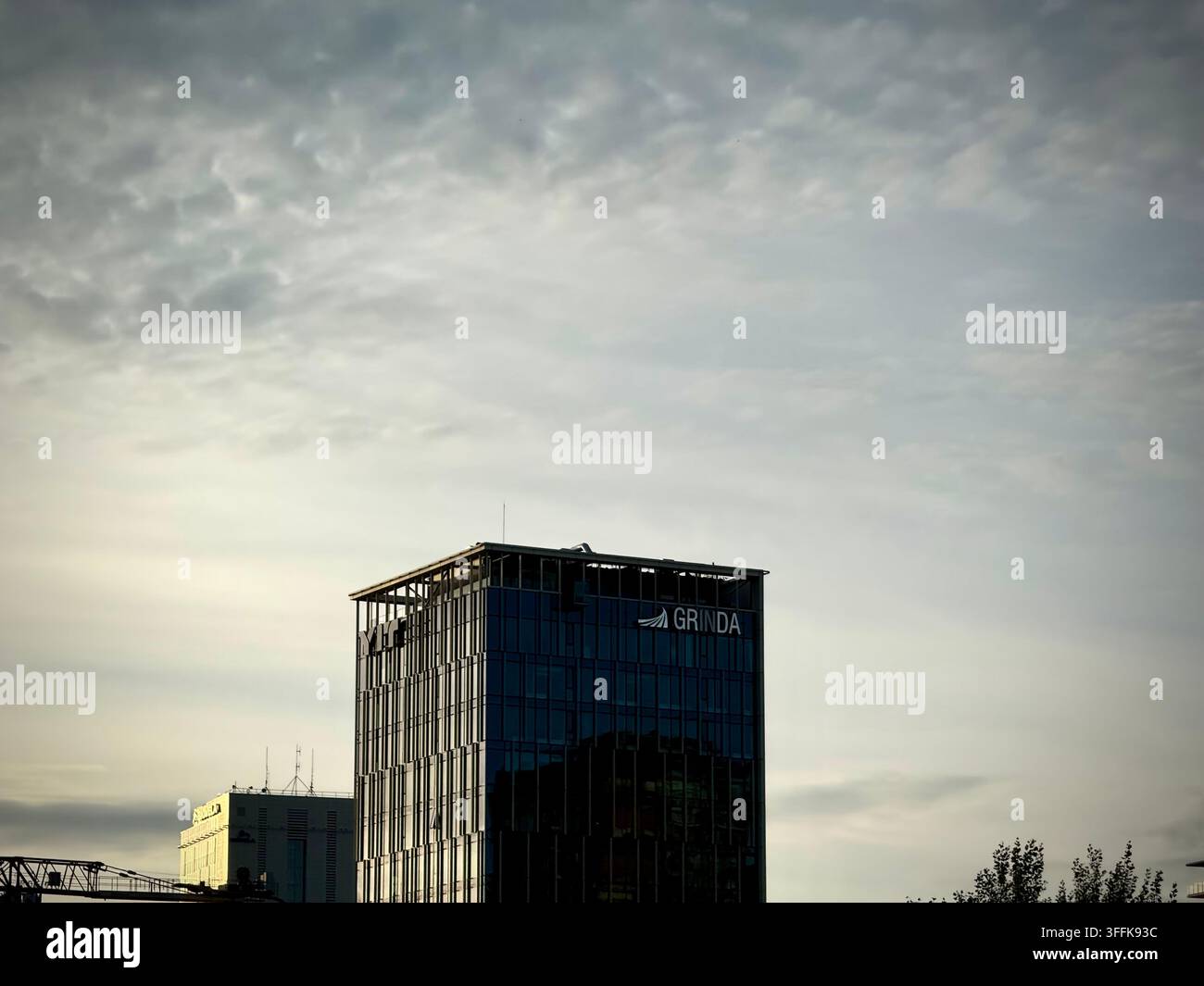 Foto ad angolo basso di un grattacielo moderno in vetro a Vilnius con il cartello aziendale Grinda sotto un cielo pieno di nuvole. - Immagine stock catturata con smartphone