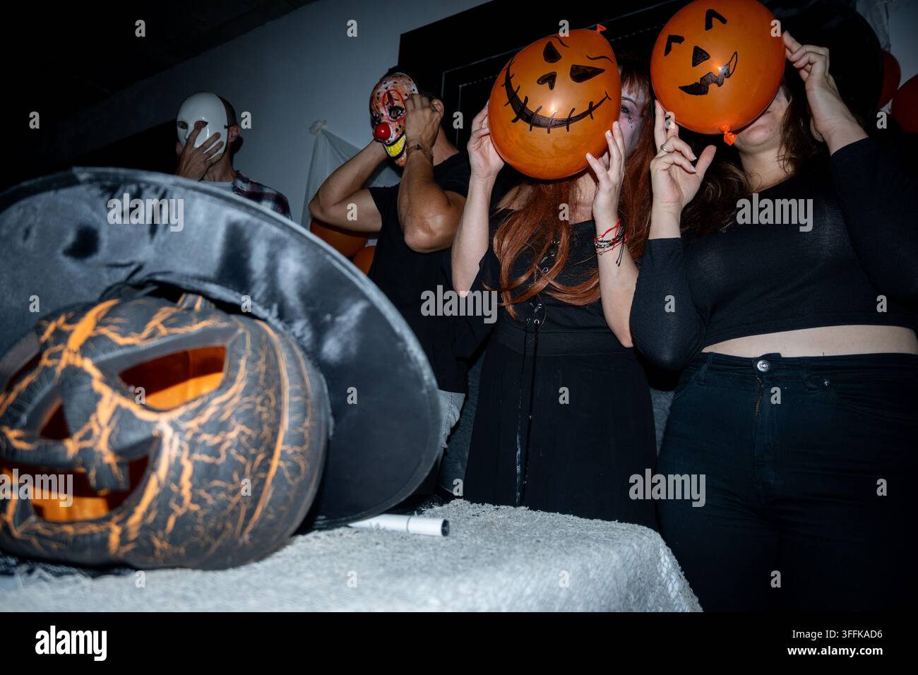 Gruppo di amici in costume che si divertono e si coprono il viso con palloncini a forma di zucca arancioni durante una celebrazione di Halloween. Foto Stock